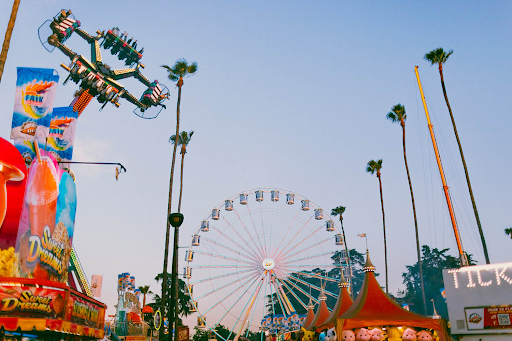 la county fair in panoma A colorful, wide-angle view of the Los Angeles County Fair featuring spinning carnival rides, large crowds of families exploring food stalls, and bright festival banners under a clear blue sky.