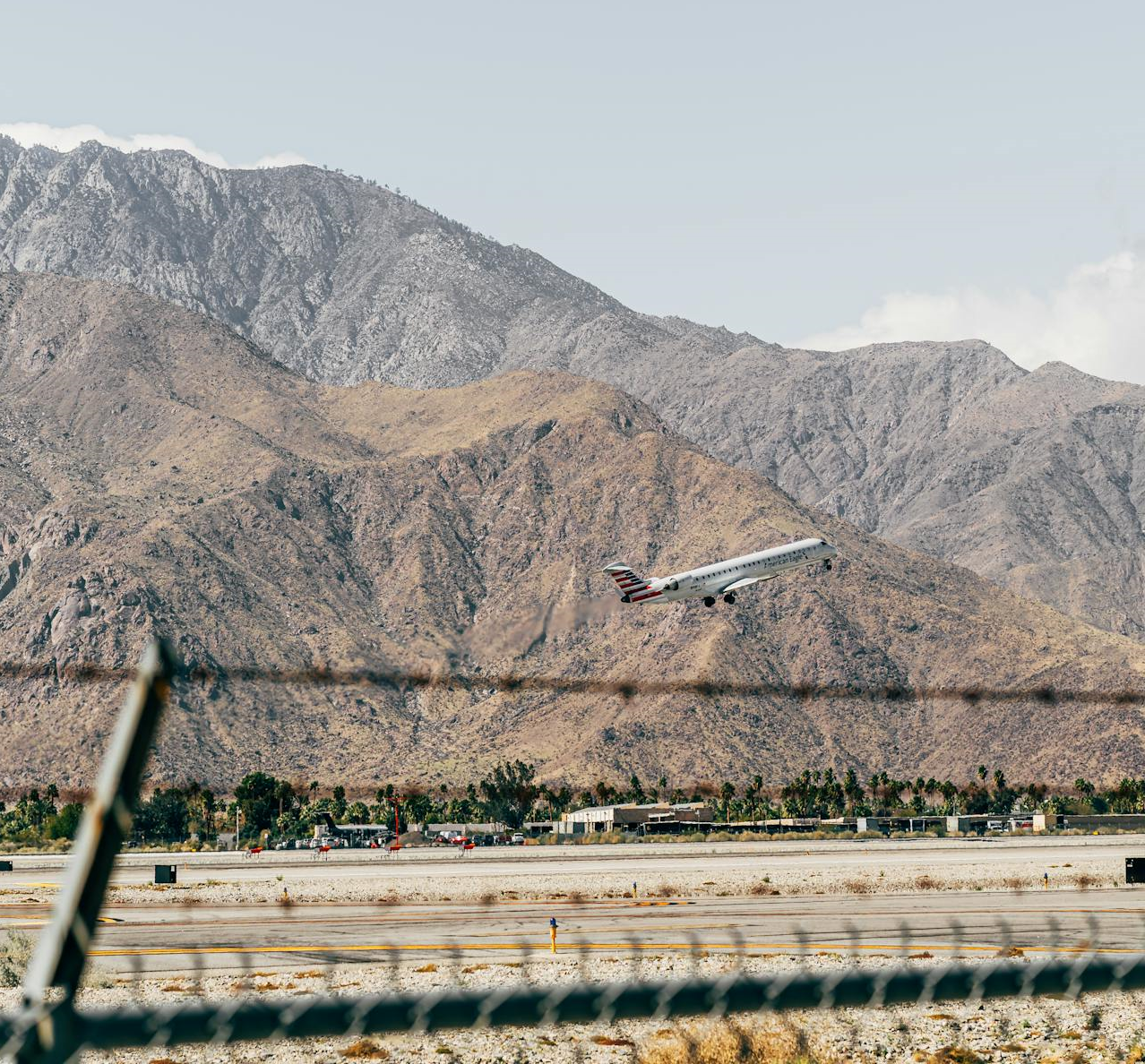 palm-springs-airport-airplane-takeoff A commercial airplane takes off from a runway into a clear, serene blue sky with a dramatic backdrop of rugged desert mountains, highlighting the unique scenery near Palm Springs Airport (PSP).