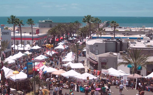 port-of-los angeles High-angle view of a crowded outdoor festival at Fiesta Hermosa in Hermosa Beach, featuring numerous white vendor tents, palm trees, and the Pacific Ocean in the background.