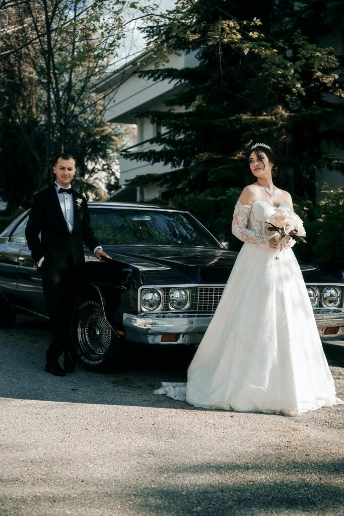 Elegant bride and groom stepping out of a luxury black car, holding her bouquet in a wedding setting.