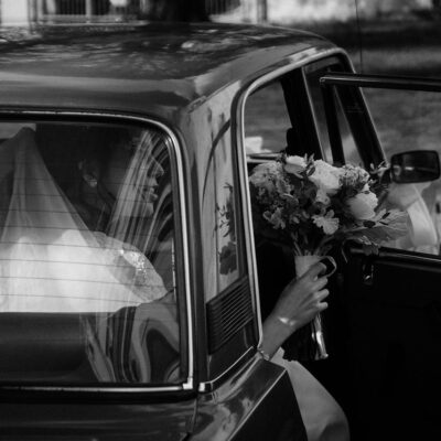 Elegant bride stepping out of a luxury black car, holding her bouquet in a wedding setting.