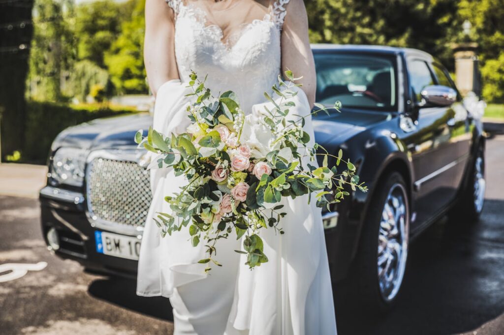 Elegant bride walking away from a luxury black car, holding her bouquet in a wedding setting.