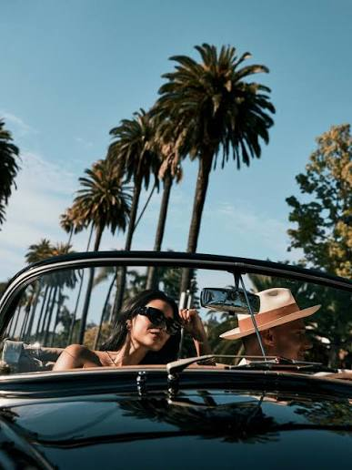 Couple riding in a luxury convertible lined with palm trees during a Southern California summer road trip with LA VIP Car Service.